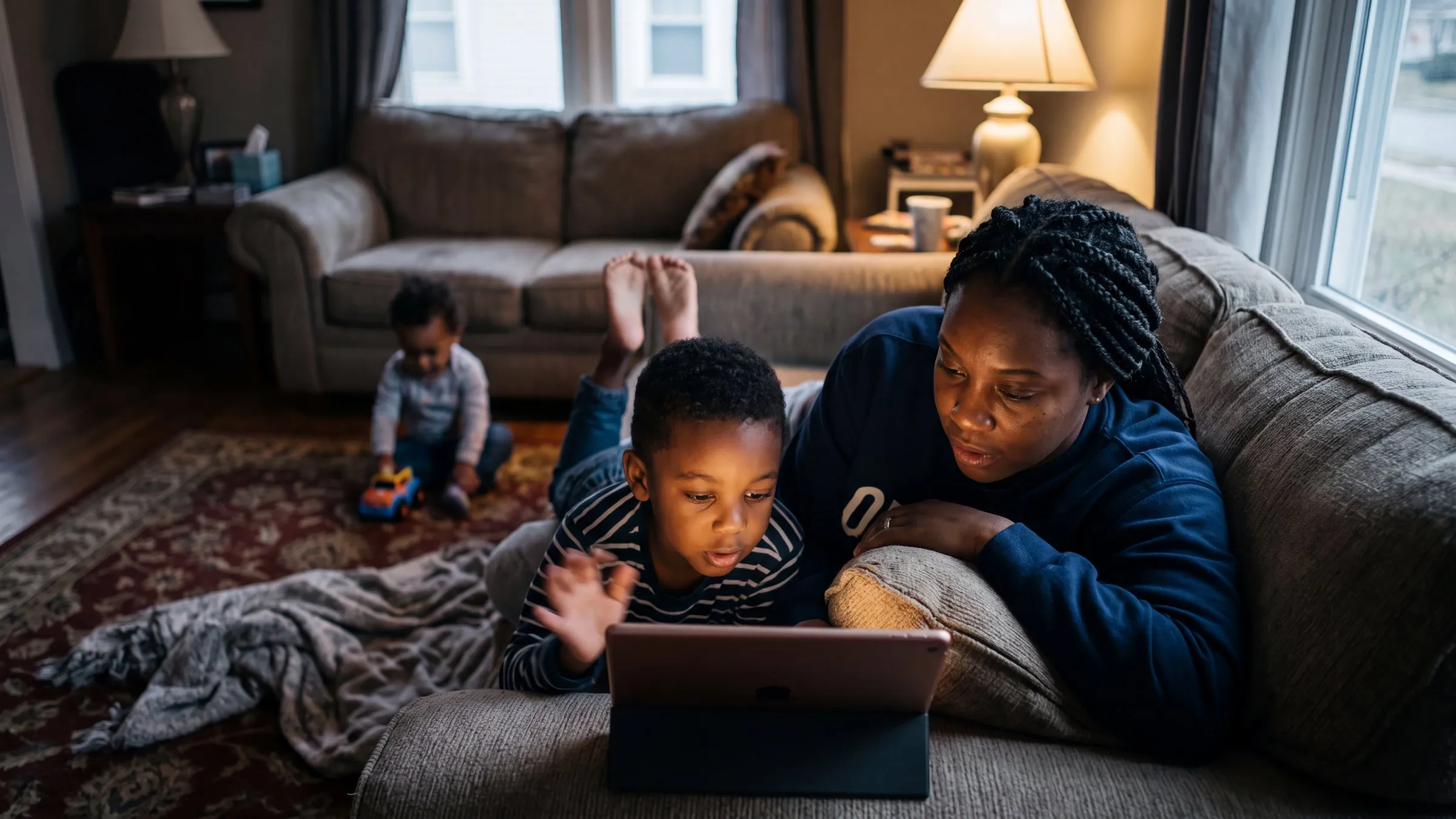 A mom and her son using an iPad on the couch in the evening